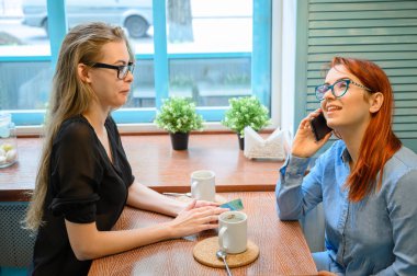 İki kız arkadaş bir kafede oturuyor ve telefonda sohbet ediyorlar. İki kadın kahve içiyor, gülümsüyor ve konuşuyor..