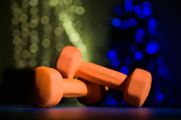 Dva sportovní činky na černém stole na pozadí vánočních světel na vánoční stromeček. — Stock fotografie