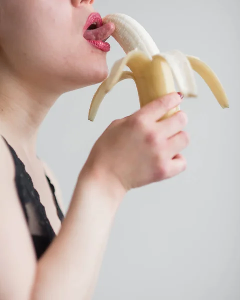 Una chica con el pelo largo y rubio lame sexualmente un plátano amarillo grande con la lengua. Es sexo oral —  Fotos de Stock
