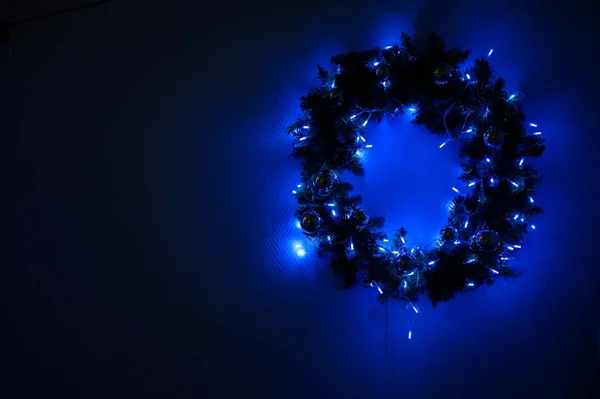 Grinalda de Natal decorado com luzes penduradas na parede em um estúdio escuro. A grinalda brilha antes do ano novo . — Fotografia de Stock