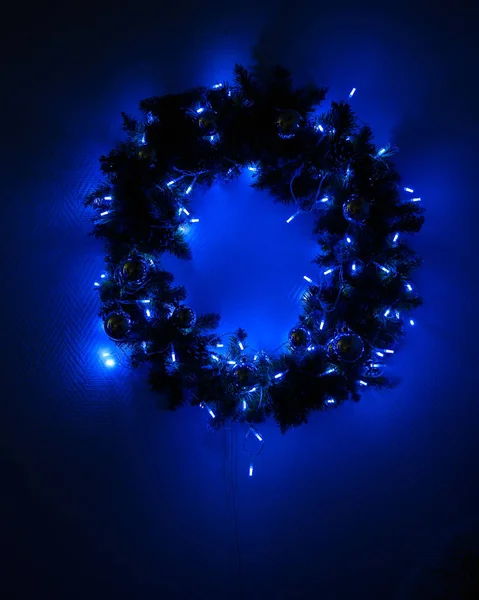 Grinalda de Natal decorado com luzes penduradas na parede em um estúdio escuro. A grinalda brilha antes do ano novo . — Fotografia de Stock
