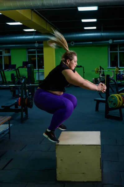 Надмірна вага жінки стрибає на коробці. Злоякісна блондинка намагається схуднути в круговому тренуванні . — стокове фото