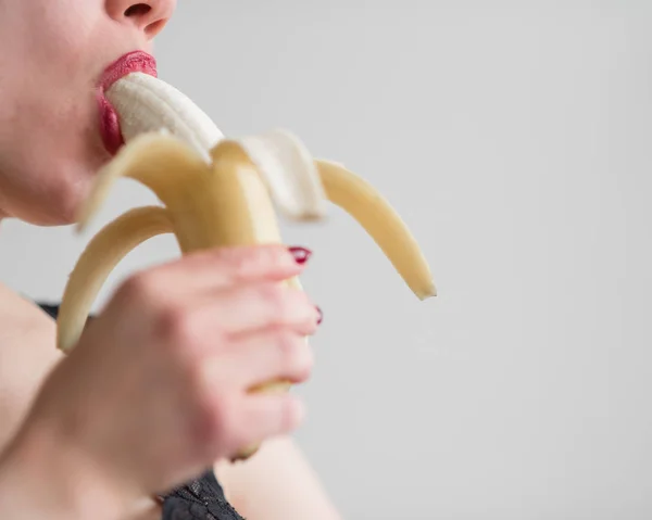 Une fille aux longs cheveux blonds lèche sexuellement une grosse banane jaune avec sa langue. Est le sexe oral — Photo