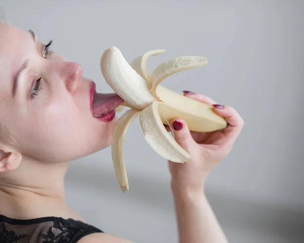 Une fille aux longs cheveux blonds lèche sexuellement une grosse banane jaune avec sa langue. Est le sexe oral — Photo