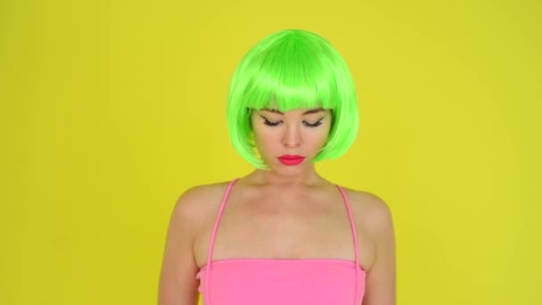 Beautiful woman in a green short wig and pink bikini posing on a yellow background. Portrait of a girl with sensual red lips. — Stock Video