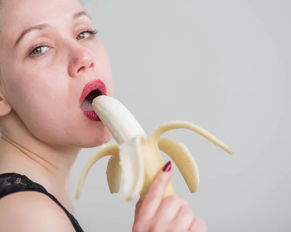 Uma menina com longos cabelos loiros lambe sexualmente uma grande banana amarela com a língua. É sexo oral — Fotografia de Stock