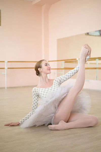 Schöne Ballerina in Körper und weißem Tutu trainiert in einem Tanzkurs. Junge flexible Tänzerin posiert in Spitzenschuhen auf dem Boden sitzend. — Stockfoto