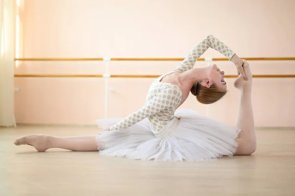 Prachtige ballerina in lichaam en witte tutu traint in een dansles. jonge flexibele danser poseren in pointe schoenen zitten op de vloer. — Stockfoto