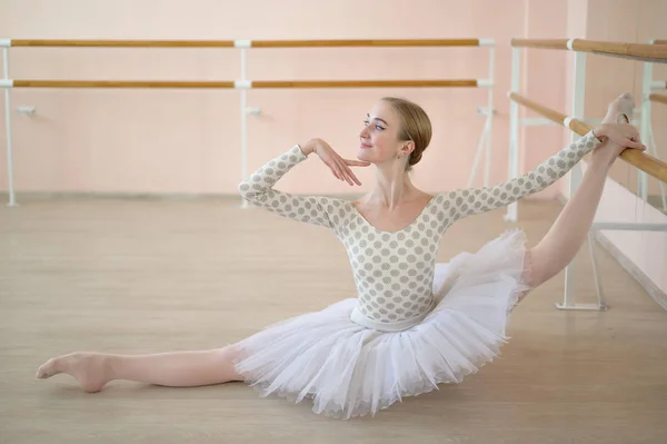 Gyönyörű balerina a testben és fehér tütü gyakorló tánc osztály és ül a spárgák. Fiatal rugalmas táncos pózol pointe cipő. — Stock Fotó