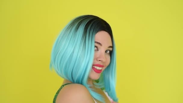 Retrato de uma menina encantadora em uma peruca azul e biquíni posando em um fundo amarelo. Mulher com cabelo artificial sorri e coloca em óculos de sol . — Vídeo de Stock