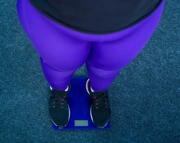 Товста жінка важить у спортзалі. Вид зверху на жіночі ноги в кросівках на електронних масштабах. ожиріння . — стокове фото