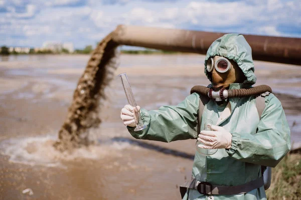Ein männlicher Umweltschützer in Schutzanzug und Gasmaske entnimmt eine Wasserprobe. Wissenschaftler bei toxikologischen Untersuchungen — Stockbild Ein männlicher Umweltschützer in Schutzanzug und Gasmaske entnimmt eine Wasserprobe. Wissenschaftler bei toxikologischen Untersuchungen. — Stockfoto