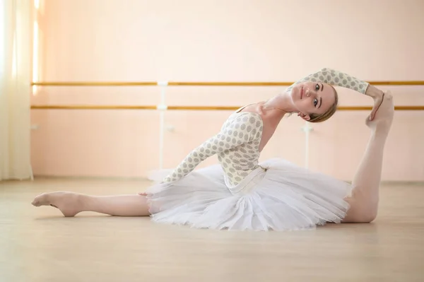 Schöne Ballerina im Körper und weißes Tutu, das im Tanzkurs übt und im Spagat sitzt. junge flexible Tänzerin posiert in Spitzenschuhen. — Stockfoto