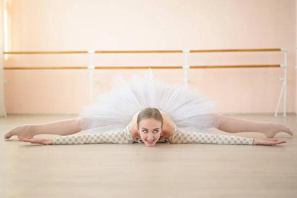 Beautiful ballerina in body and white tutu is training in a dance class. Young flexible dancer posing in pointe shoes sitting on the floor. — Stock Photo, Image