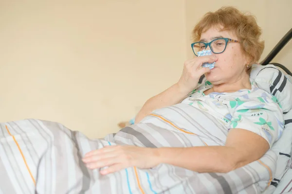 An elderly woman suffers from the flu and runny nose. The pensioner blows her nose in the nasal raft. — 스톡 사진