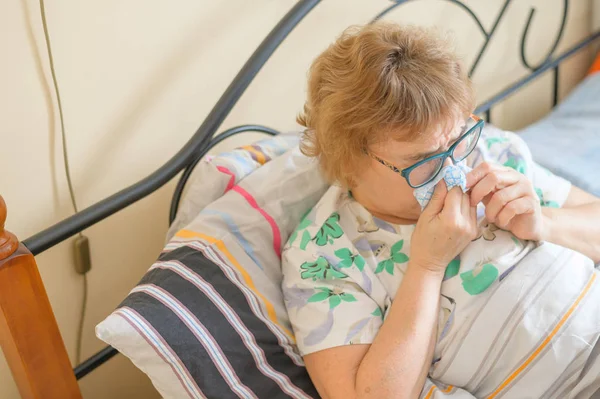 An elderly woman suffers from the flu and runny nose. The pensioner blows her nose in the nasal raft. — 스톡 사진