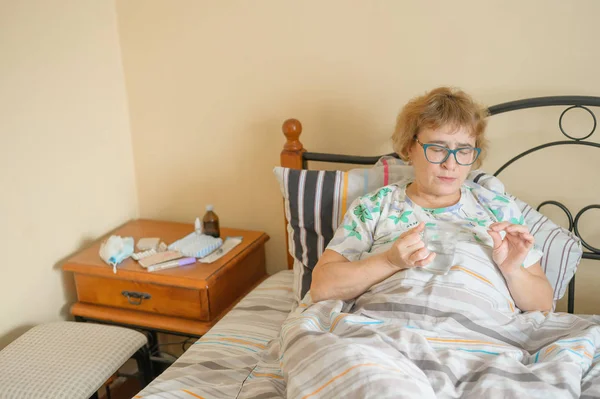 Sick old woman is lying at home in bed. A pensioner takes a cure for the disease and drinks a glass of water.