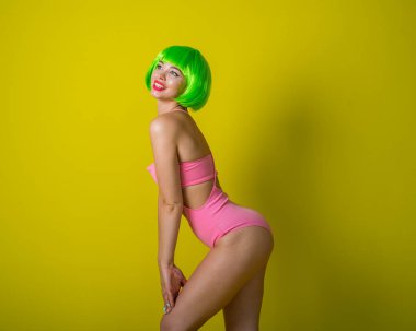 Yeşil kısa peruklu, pembe bikinili, sarı arka planda poz veren güzel kadın. Şehvetli kırmızı dudaklı bir kızın portresi..