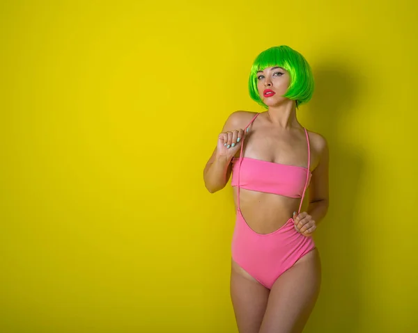 Красивая женщина в зелёном коротком парике и розовом бикини позирует на жёлтом фоне. Портрет девушки с чувственными красными губами . — стоковое фото