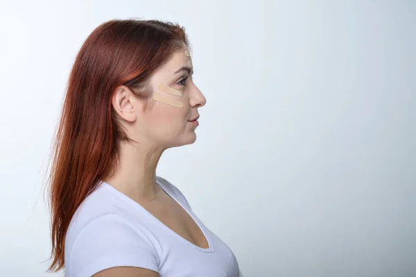 Perfil mujer pelirroja con cinta adhesiva en la piel rejuvenecimiento de la tez. Una forma alternativa de combatir las arrugas . — Foto de Stock