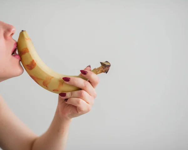 Close-up do rosto, lábios, língua de uma jovem, menina europeia lambendo uma grande banana amarela, doce . — Fotografia de Stock