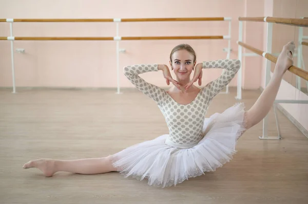 Balerina indah dalam tubuh dan tutu putih adalah pelatihan di kelas tari. Muda penari fleksibel berpose dalam sepatu runcing duduk di lantai. — Stok Foto