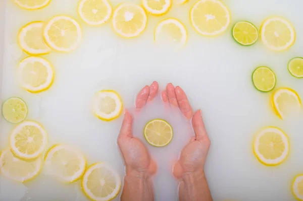 Une tranche de citron vert mûr dans les mains d'une femme. Vue de dessus Fille prend un bain de lait avec des citrons. Spa aux agrumes . — Photo