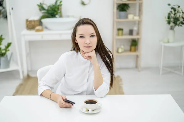 Eine Frau im weißen Hemd trinkt Kaffee in einem Café. Eine Büroangestellte in der Mittagspause löst telefonisch ein Geschäftsproblem. Manager auf mittlerer Ebene — Stockfoto