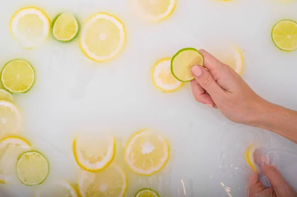 Une tranche de citron vert mûr dans les mains d'une femme. Vue de dessus Fille prend un bain de lait avec des citrons. Spa aux agrumes. Soins du corps. Blanchiment de la peau . — Photo