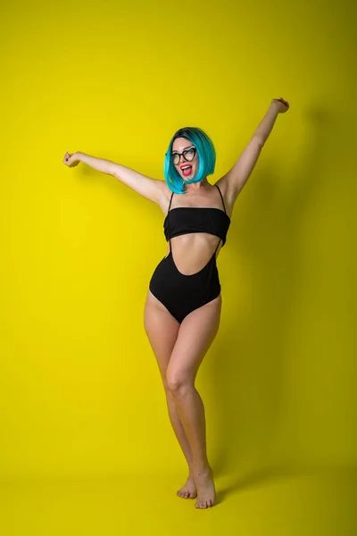 Hermosa mujer en bikini negro con peluca de colores y gafas de sol sobre fondo amarillo. Chica posando en el estudio . —  Fotos de Stock