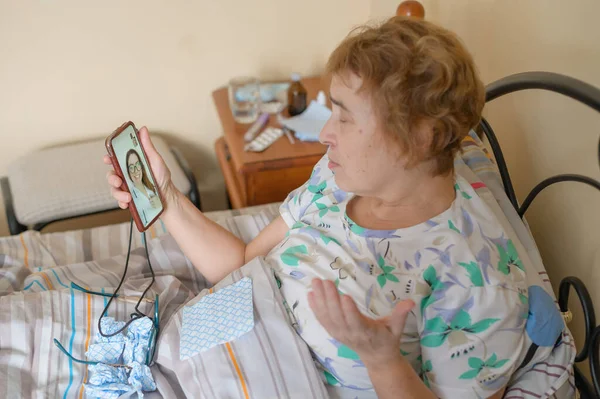 Μια ηλικιωμένη γυναίκα μιλάει με τον γιατρό στο τηλέφωνο. Ένας συνταξιούχος πάσχει από αναπνευστική νόσο και κάνει βιντεοκλήση στον θεραπευτή. Ηλεκτρονική διαβούλευση — Φωτογραφία Αρχείου