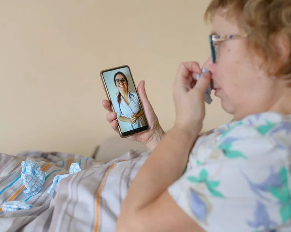 An elderly woman talking to the doctor on the phone. A pensioner suffers from a respiratory illness and makes a video call to the therapist. Online consultation