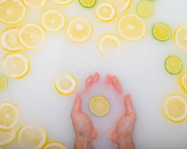 A slice of ripe lime in the hands of a woman. Top view Girl takes a milk bath with lemons. Citrus spa. — Stock Photo, Image