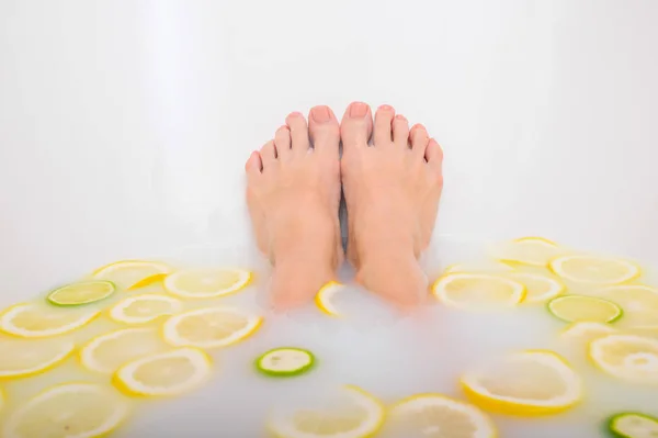 Mädchen nimmt ein Milchbad mit Zitronen und Limetten. Zitrusbad. Körperpflege. Hautaufhellung. Frauenbeine. — Stockfoto