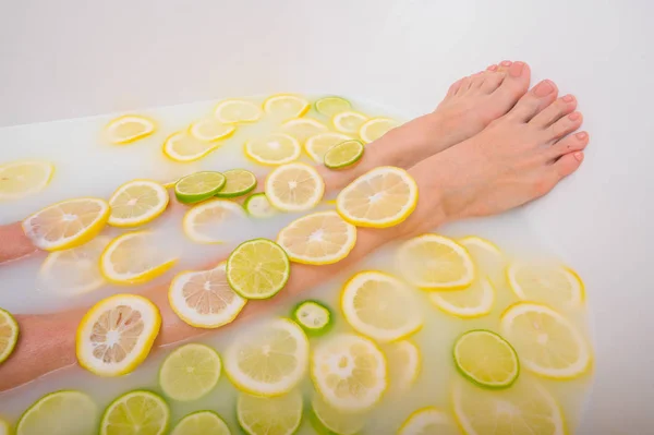 Fille prend un bain de lait avec des citrons et des citrons verts. Spa aux agrumes. Soins du corps. Blanchiment de la peau. Jambes de femmes . — Photo