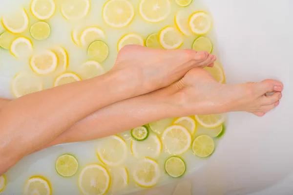 Mujer irreconocible toma un baño de leche con limones y limas. Spa cítrico. Cuidado corporal. Blanqueamiento de la piel. piernas femeninas vista superior. — Foto de Stock