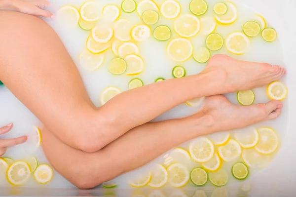 Donna irriconoscibile si fa un bagno al latte con limoni e lime. Citrus spa. Cura del corpo. Sbiancamento della pelle. Gambe femminili vista dall'alto. — Foto Stock