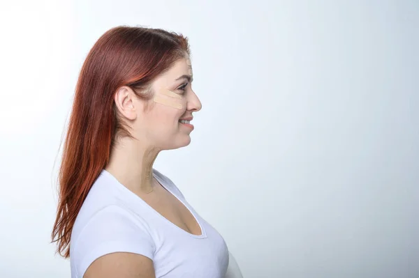 Perfil mujer pelirroja con cinta adhesiva en la piel rejuvenecimiento de la tez. Una forma alternativa de combatir las arrugas . — Foto de Stock