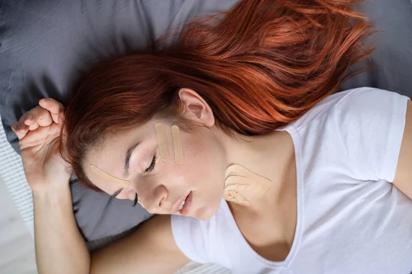 Fita Kineyzio no rosto de uma menina adormecida. Uma mulher está deitada em uma cama com manchas para rejuvenescimento facial . — Fotografia de Stock