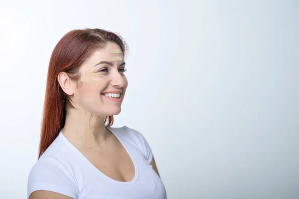 Retrato de una mujer pelirroja con cintas en la cara de color de piel para el rejuvenecimiento. Una forma alternativa de combatir las arrugas . — Foto de Stock