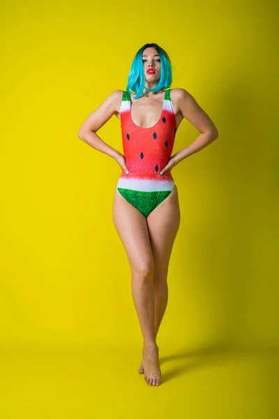 Portrait of a woman in a swimsuit with a picture of a watermelon. Stylish girl in a colored short wig posing in the studio on a yellow background. — 스톡 사진