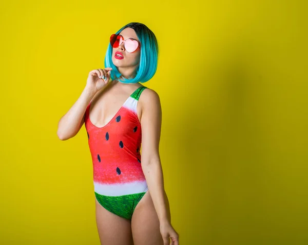 Portrait of a woman in a swimsuit with a picture of a watermelon. Stylish girl in a colored short wig posing in the studio on a yellow background. — 스톡 사진