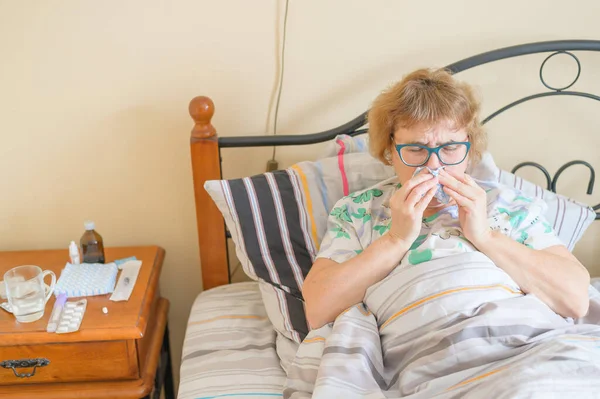 Μια ηλικιωμένη γυναίκα πάσχει από γρίπη και καταρροή. Η συνταξιούχος φυσάει τη μύτη της στη ρινική σχεδία.. — Φωτογραφία Αρχείου