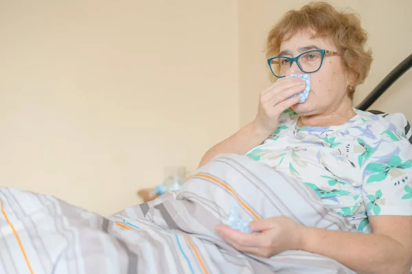 An elderly woman suffers from the flu and runny nose. The pensioner blows her nose in the nasal raft. — 스톡 사진