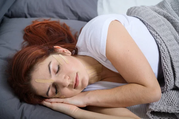 Fita do Kineyzio na cara de uma rapariga adormecida. Uma mulher está deitada numa cama com manchas para o rejuvenescimento facial. Cosmetologia alternativa . — Fotografia de Stock