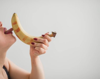 Yetişkin Avrupalı bir kız, cinsel olarak koca bir muzu yalıyor ve emiyor. Oral seks fantezileri. Yüzü yakın çekim.