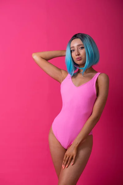 Pretty woman in a pink monokini and blue wig in the studio. Girl with artificial short hair posing in a colored swimsuit. — 스톡 사진
