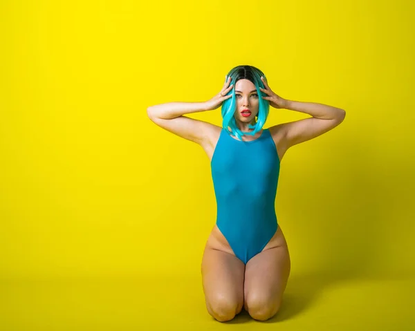 Portrait of a blue hair woman in a wig and a swimsuit on a yellow background. Fashion Girl in a monokini with artificial hair posing in the studio. — 스톡 사진