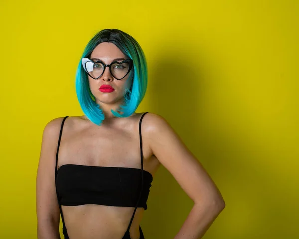 Beautiful woman in a black bikini in a colored wig and sunglasses on a yellow background. Girl posing in the studio. — 스톡 사진