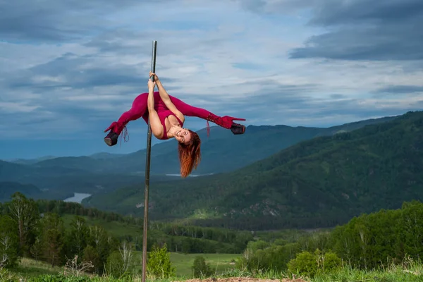 Belle femme rousse dansant sur une plate-forme portable sur un fond de montagnes. La fille se déplace sexuellement à côté du poteau. Combinaison pour les cours. talons hauts. Altaï. Grande flexibilité . — Photo